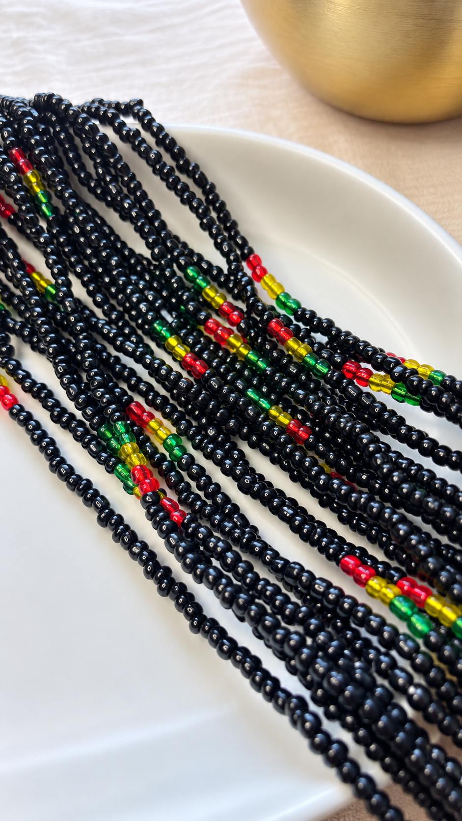 Live Ghana black, red, gold, and green waist beads arranged on a white dish