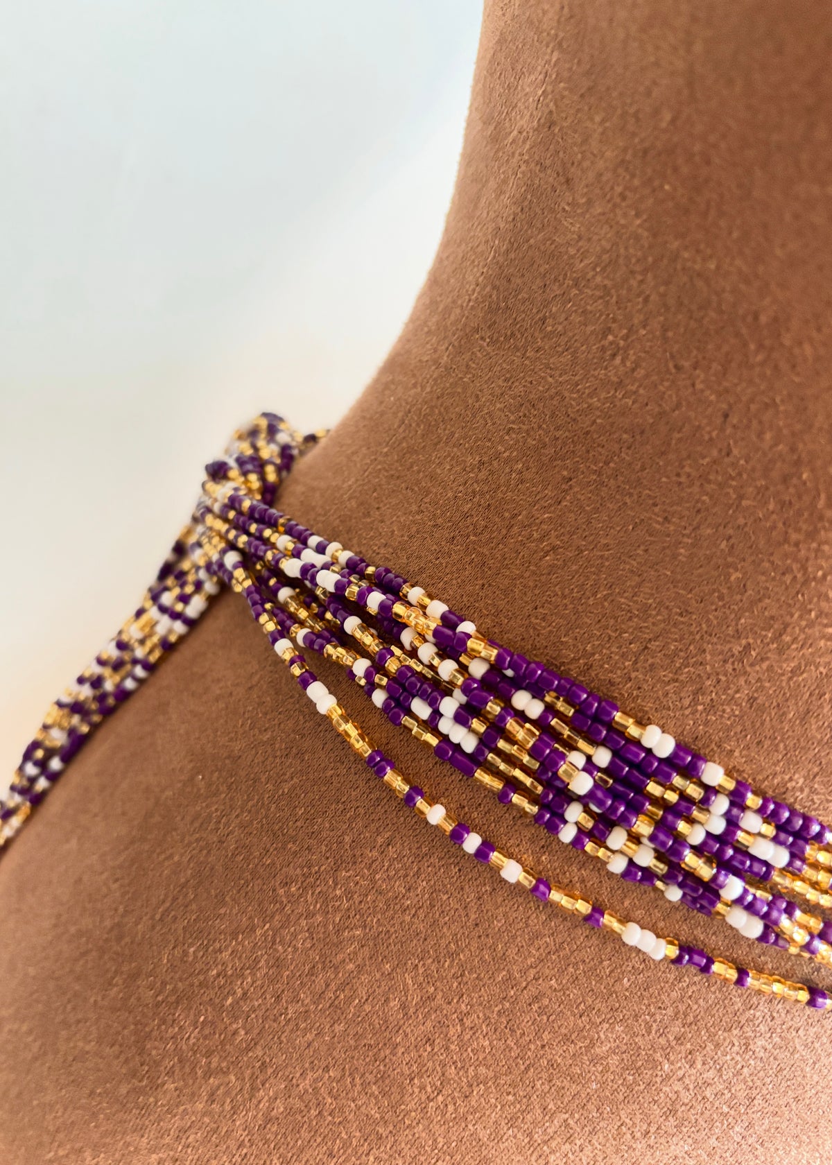 Close-up of Purple Reign waist beads in violet, gold, and white on a display form