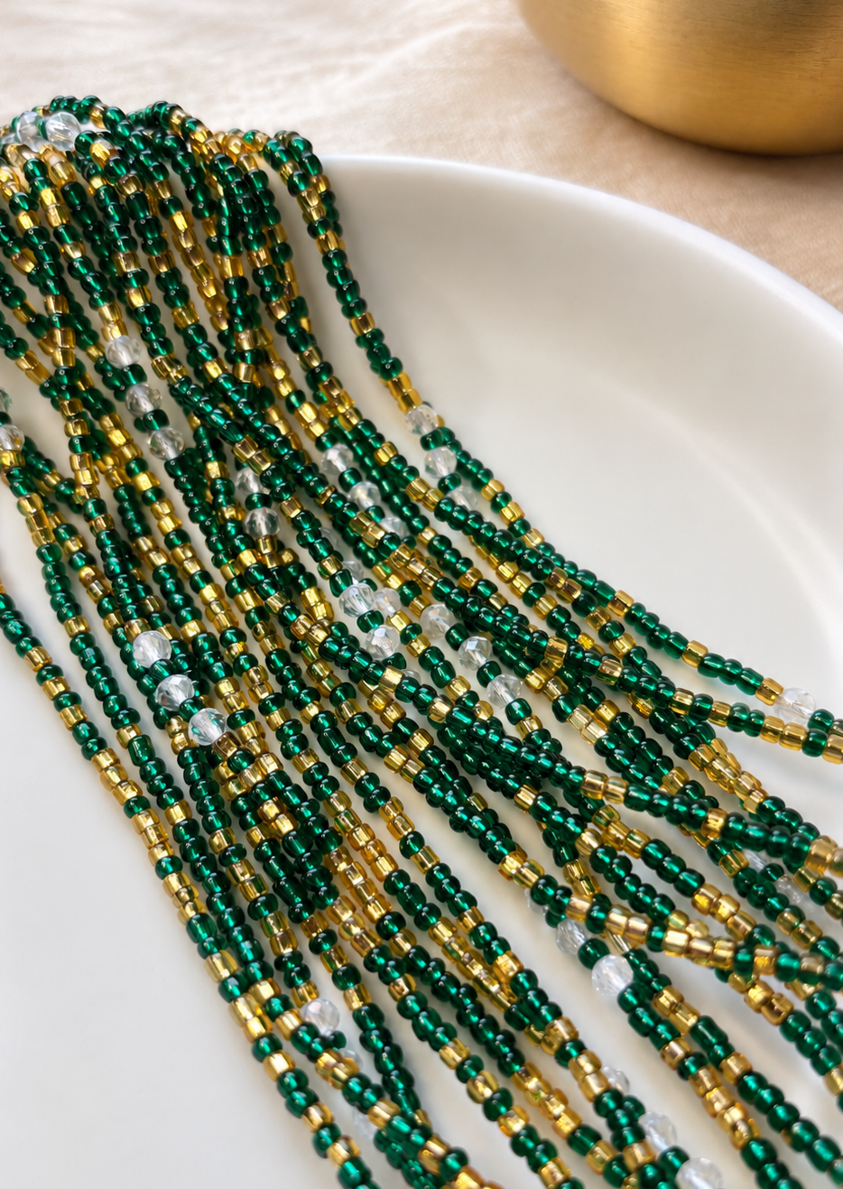 Emerald Dynasty Luxe emerald green and gold waist beads with iridescent accents arranged on a white dish