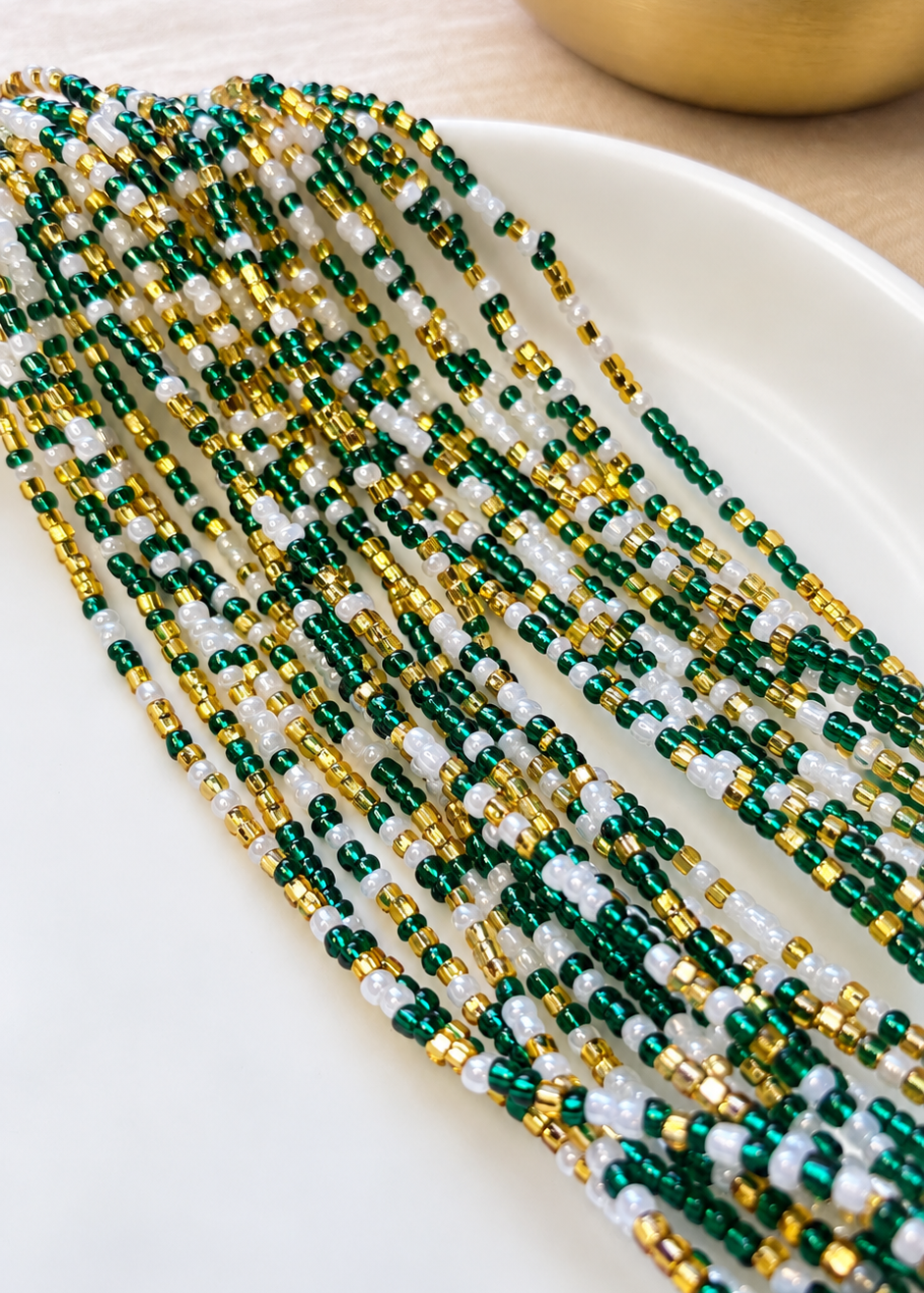 Emerald Dynasty Pearl green, gold, and pearl white waist beads arranged on a white dish