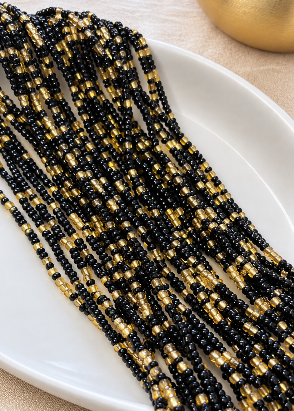 Black and gold Obaa Sima waist beads arranged on a white dish