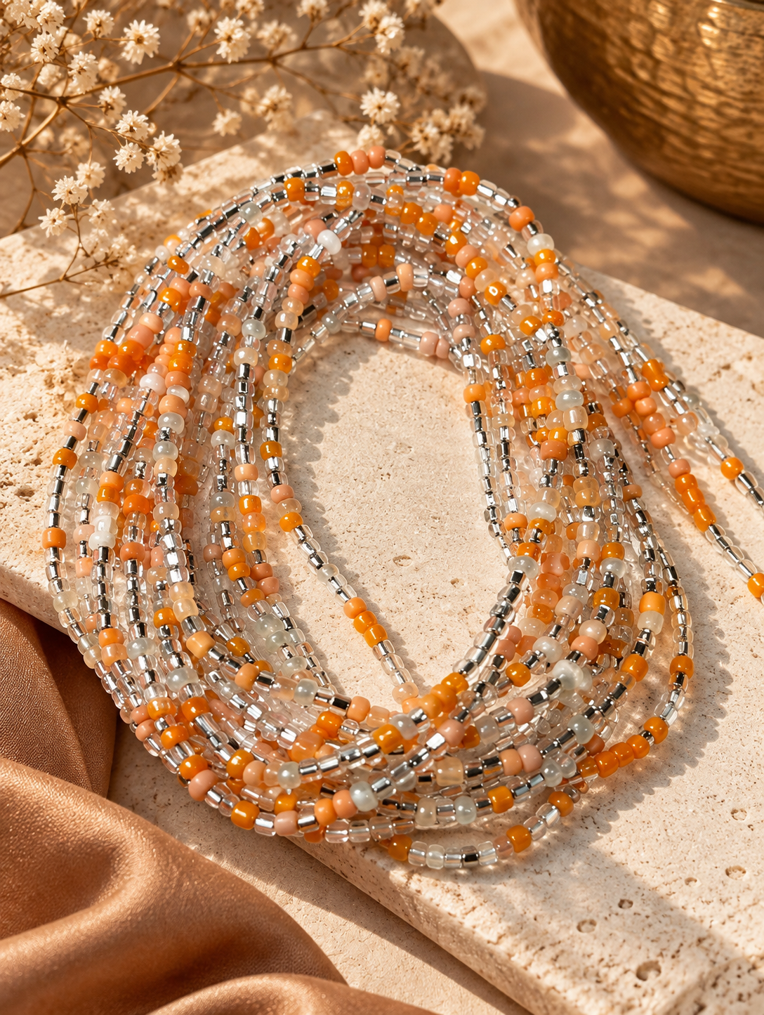Demure de Brittany waist beads in peach, pearl white, and silver tones arranged on a stone tray