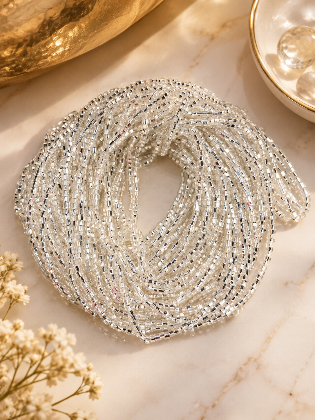 Silver Whisper waist beads arranged in a coil on a light dish