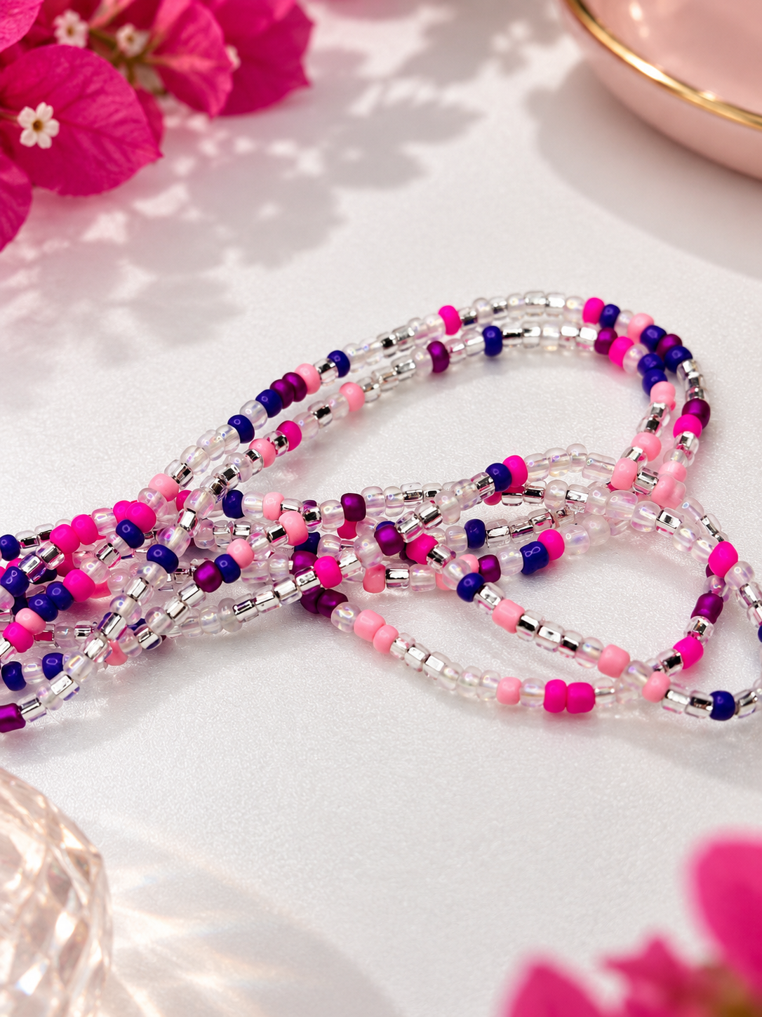 Close-up of pink, purple, and clear Pink Reign waist beads on a light surface