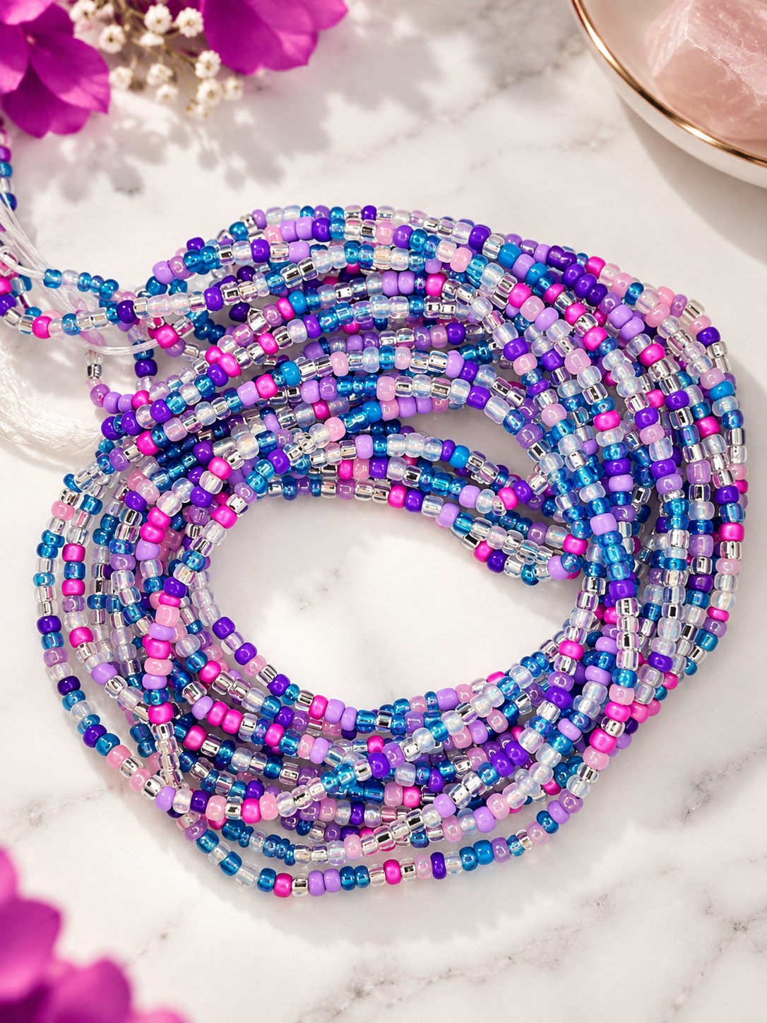 Cotton Candy waist beads in blue, lavender, pink, fuchsia, and iridescent tones arranged on a white surface