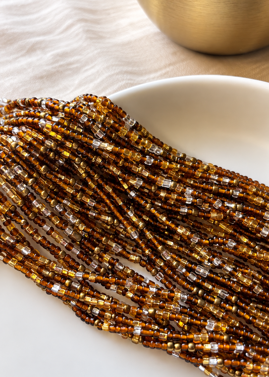 Crowned brown, gold, antique gold, and silver glass waist beads gathered on an ivory dish