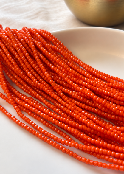Zinnia waist beads in vibrant orange, arranged in strands on a light dish.