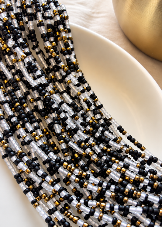 Gilded Noir clear, black, and antique gold waist beads arranged on a white dish