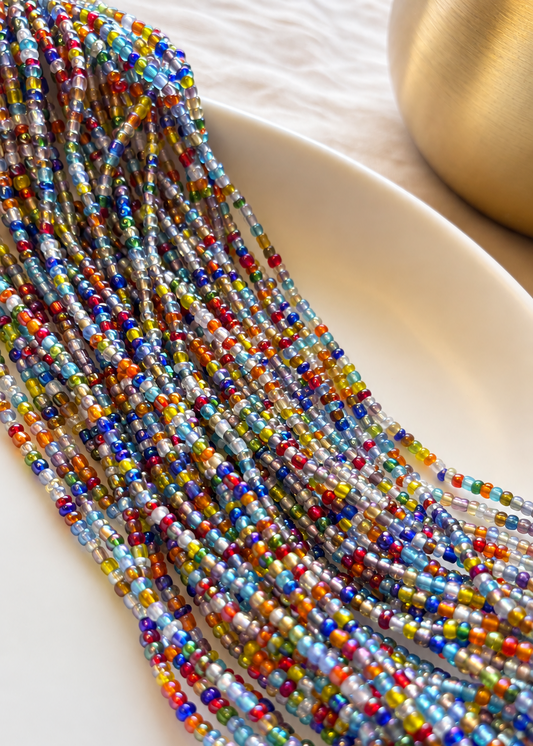 Mélange multicolor jewel-tone waist beads arranged on a white dish