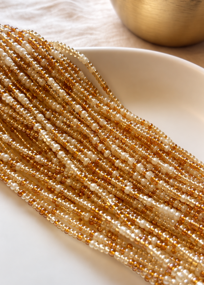 Empress champagne, warm amber, and pearl ivory waist beads arranged on a white dish