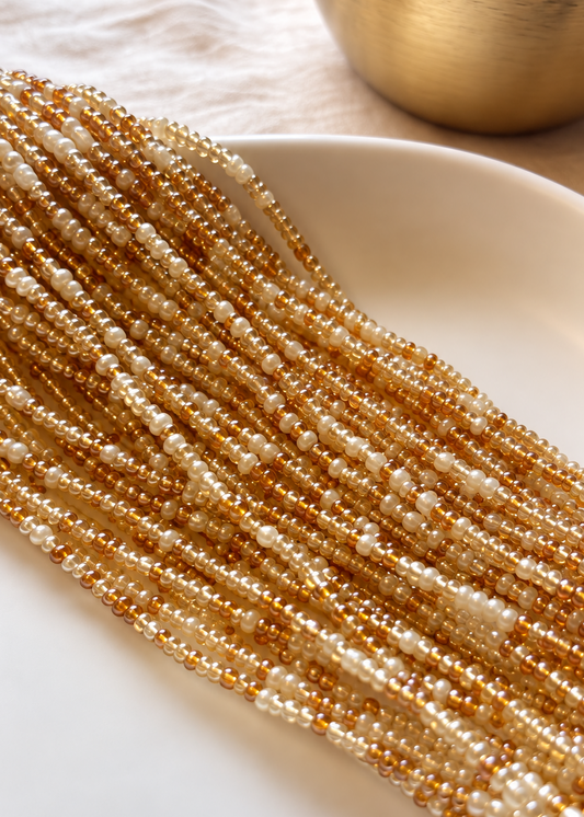 Empress champagne, warm amber, and pearl ivory waist beads arranged on a white dish