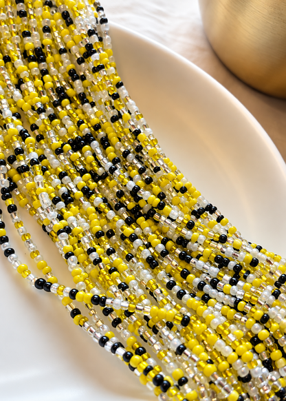 Queen Bee waist beads in yellow, black, silver, and pearl white arranged on a dish