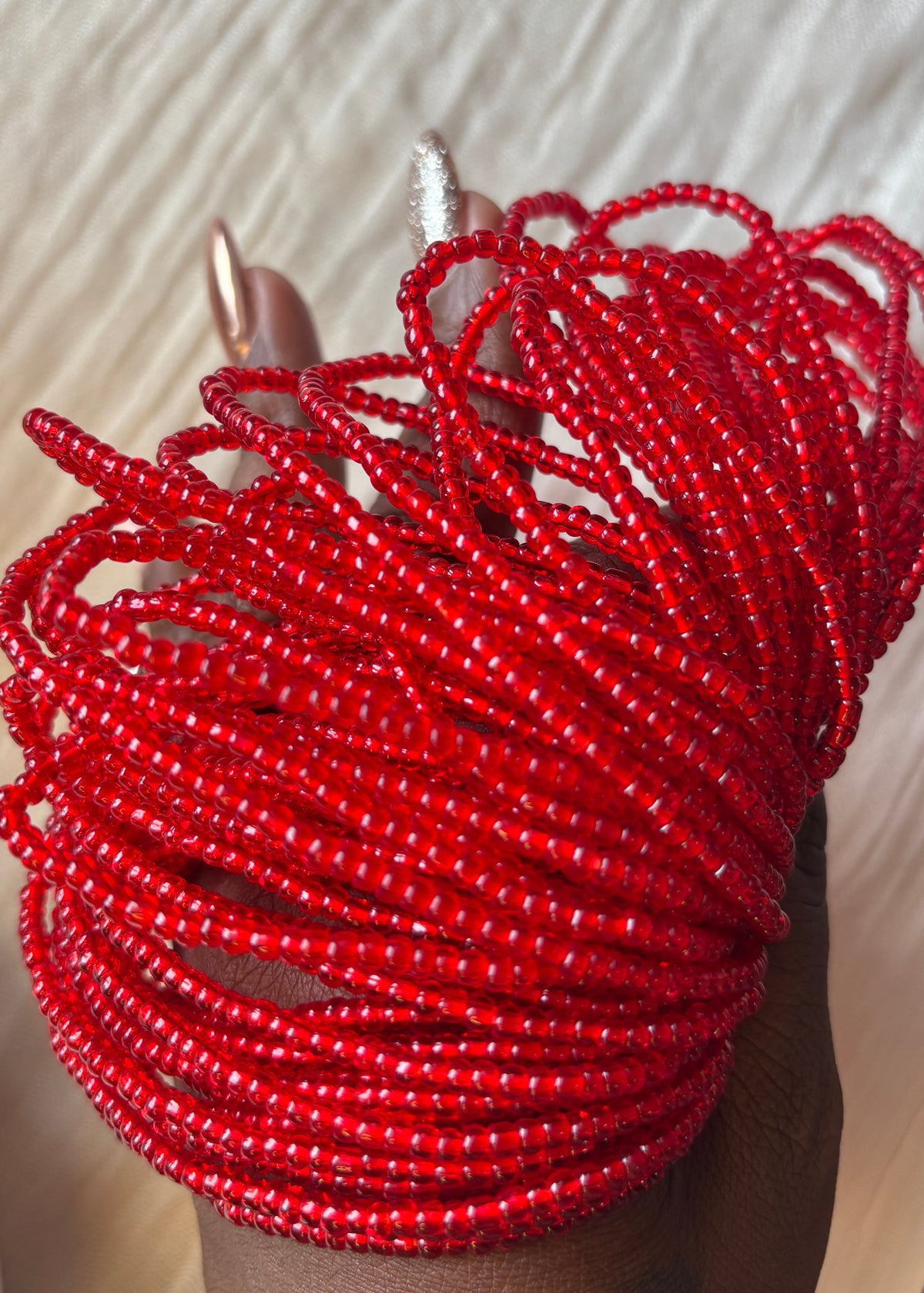 Several loops of red Mi Amor waist beads held in a hand