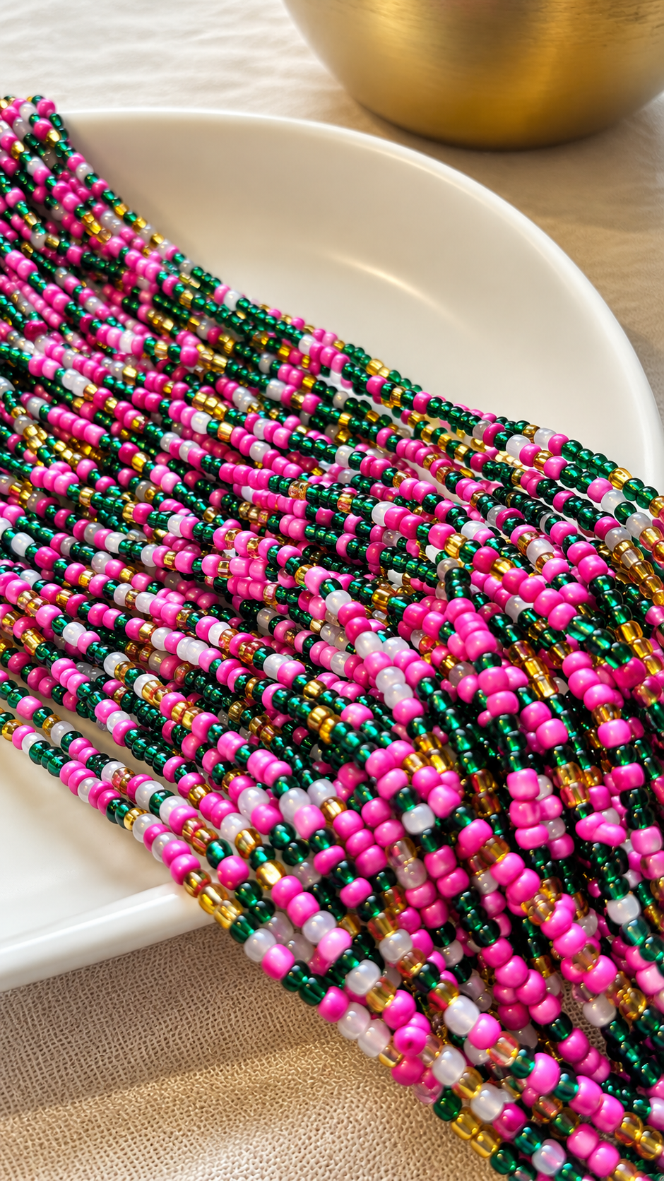 Blossom Royale emerald, fuchsia, white, and gold glass waist beads draped across an ivory dish