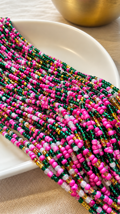 Blossom Royale emerald, fuchsia, white, and gold glass waist beads draped across an ivory dish