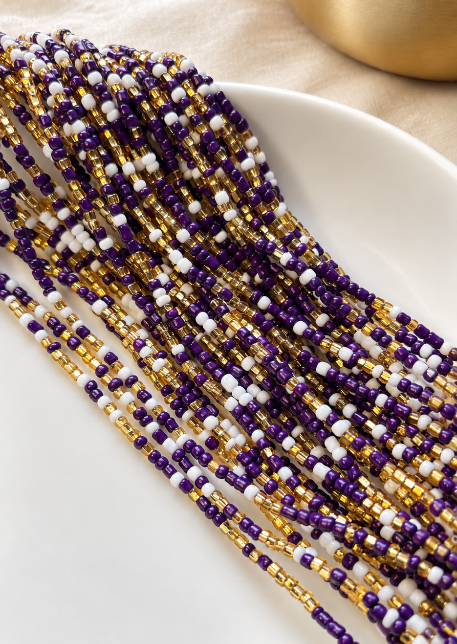 Purple Reign waist beads in violet, gold, and white arranged on a dish