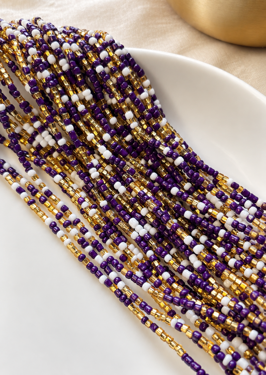 Purple Reign waist beads in violet, gold, and white arranged on a dish