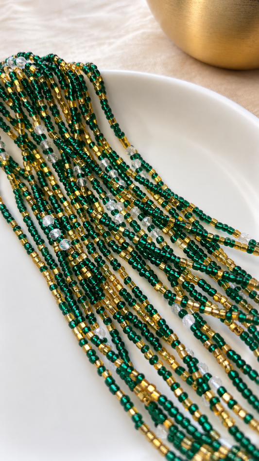Emerald Dynasty Luxe emerald green and gold waist beads with iridescent accents arranged on a white dish