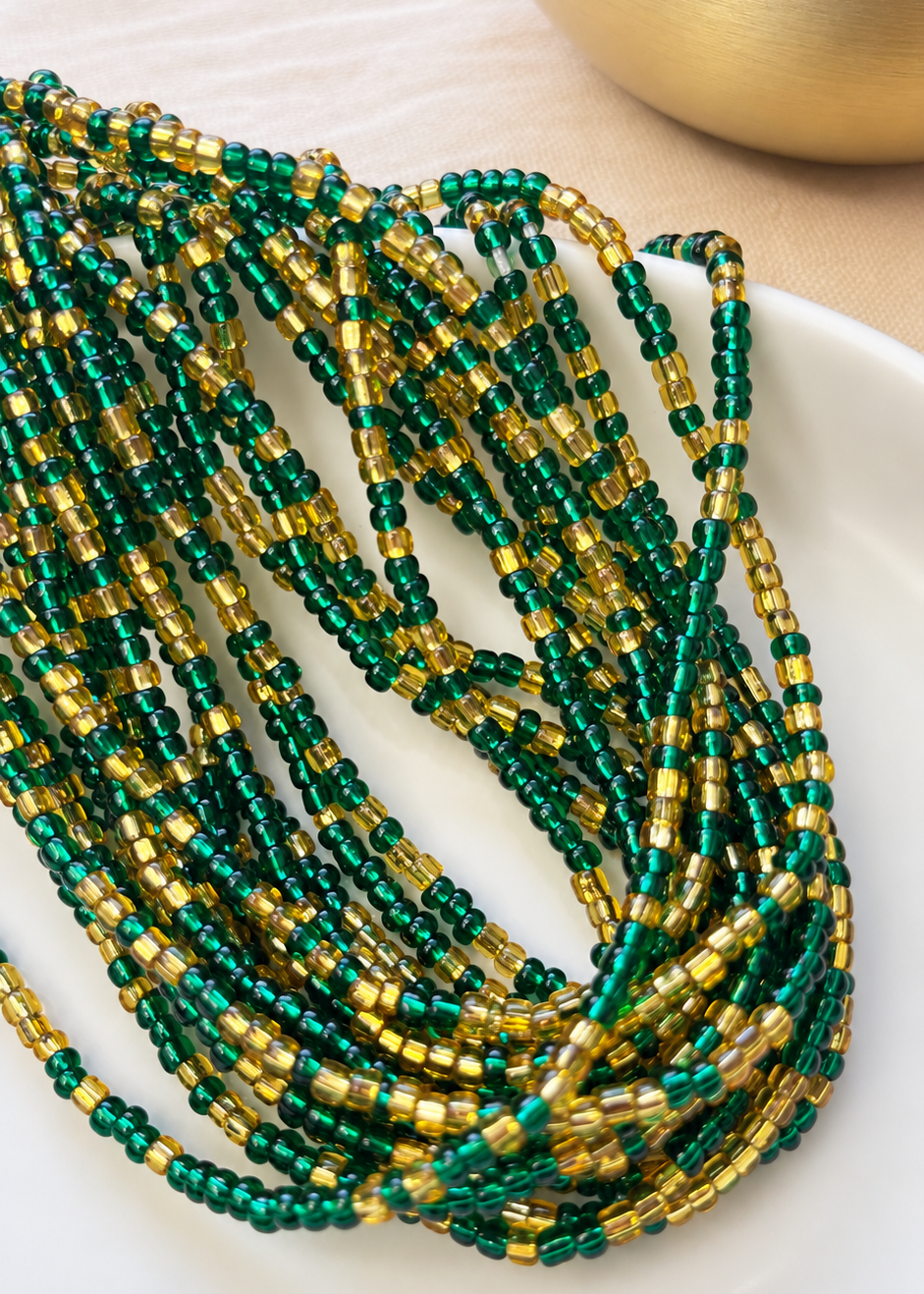 Emerald Dynasty emerald green and gold waist beads draped on a white dish