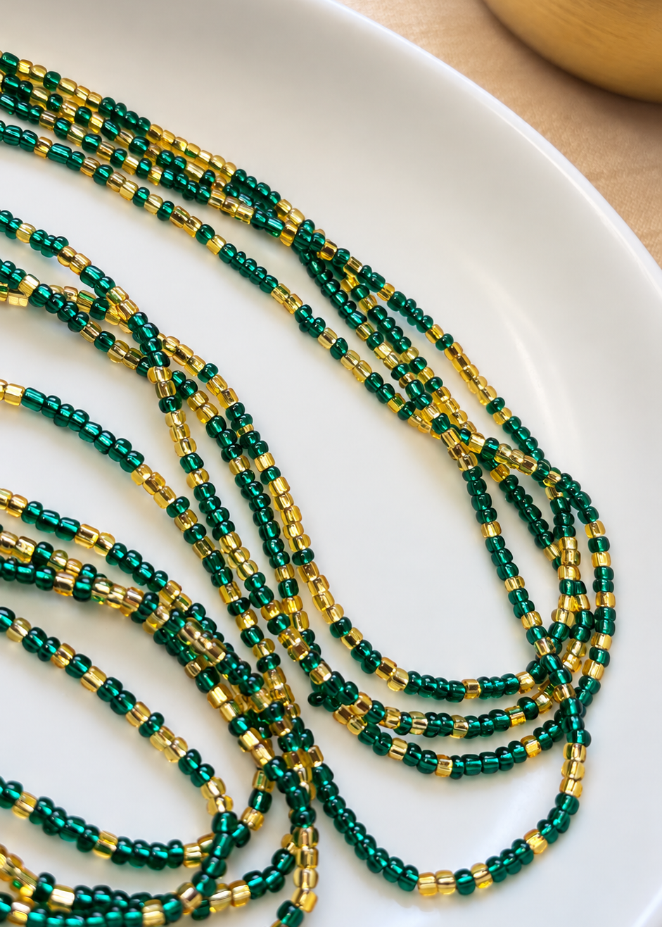 Close-up of Emerald Dynasty emerald green and gold waist beads arranged on a white dish