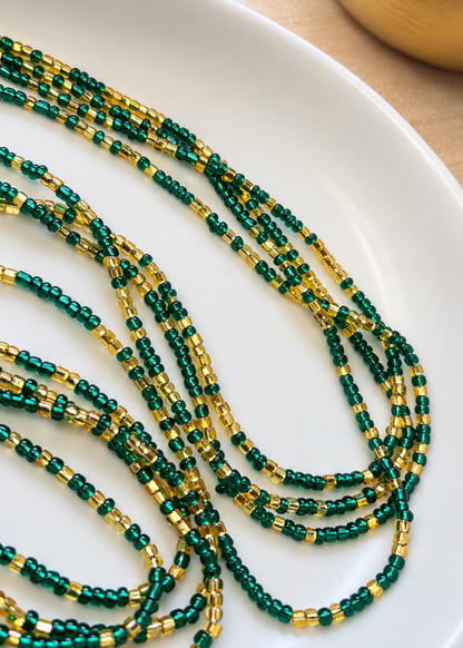Close-up of Emerald Dynasty emerald green and gold waist beads arranged on a white dish