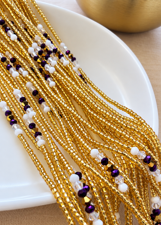 The Matriarch Luxe waist beads in gold, purple, white, and clear tones arranged on a dish