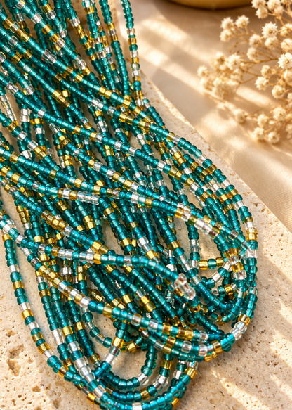 Aqua, gold, and silver Ocean Glow waist beads arranged on a light surface