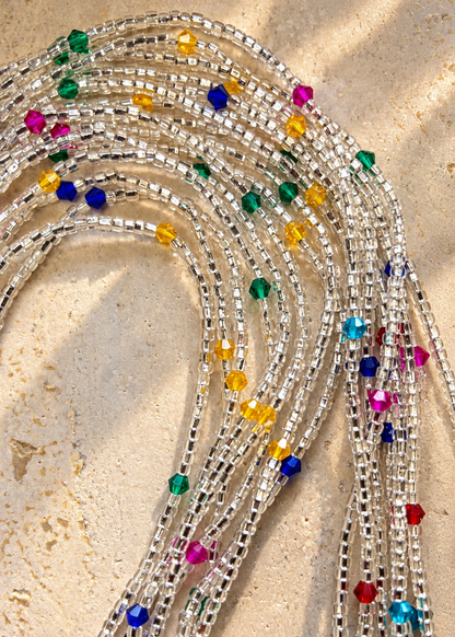 Celestial Spark Luxe waist beads arranged in loops, with silver-lined clear beads and colorful crystal accents on a light surface