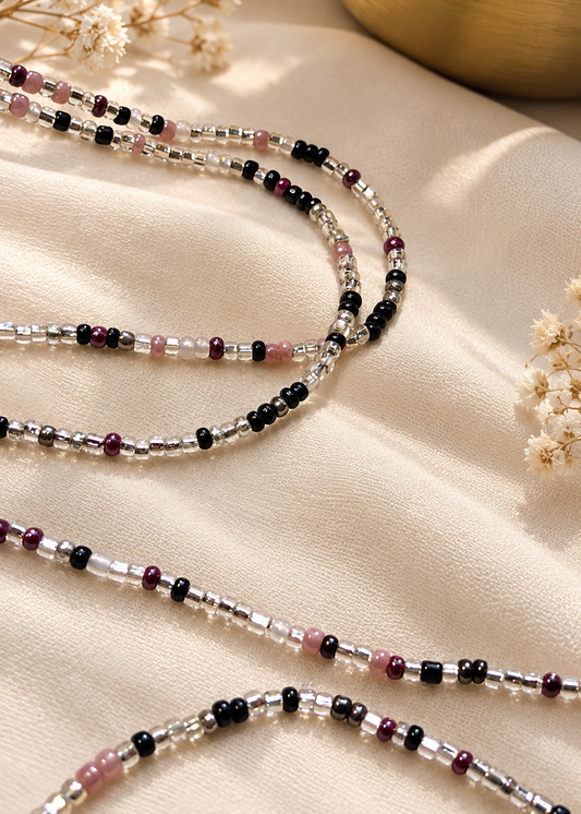 Mauve Noire waist beads in mauve, black, clear, and silver tones arranged on fabric