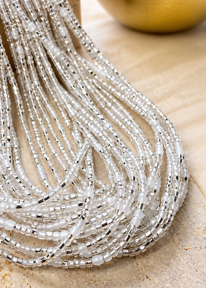 Silver and iridescent white Silver Bloom waist beads arranged on a textured surface