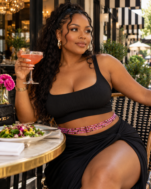 Model seated at an outdoor table wearing Charisma hot pink, black, and white waist beads