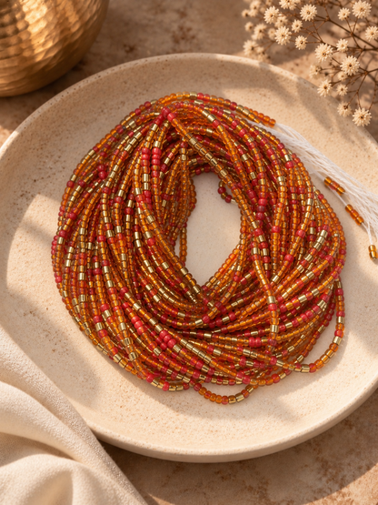 Ember Sol orange, warm red, and gold waist beads arranged on a ceramic dish