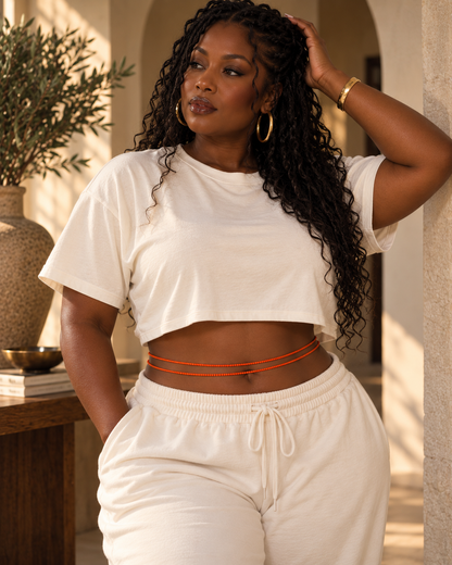Model wearing orange Zinnia waist beads with a white cropped top and matching pants.