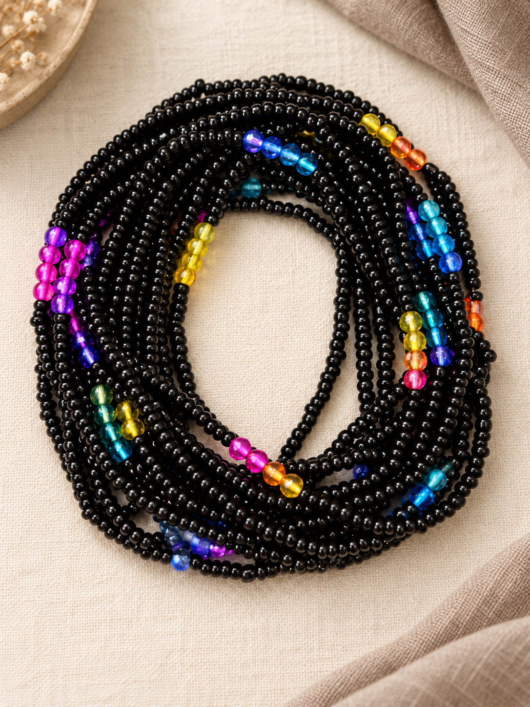 Black Unicorn black glass waist beads with colorful ombré crystal accents arranged in a coil on beige fabric