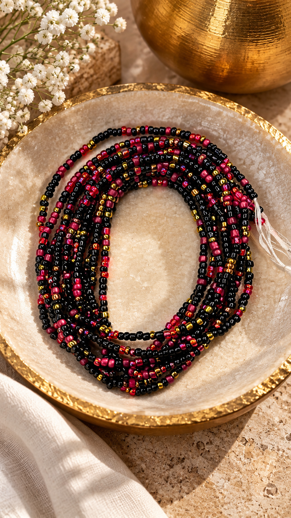 Gracious Goddess black, iridescent red, and gold waist beads arranged on a stone dish