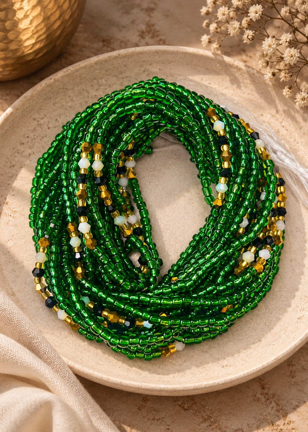 Emerald City emerald green waist beads with black, gold, and white accents arranged on a dish