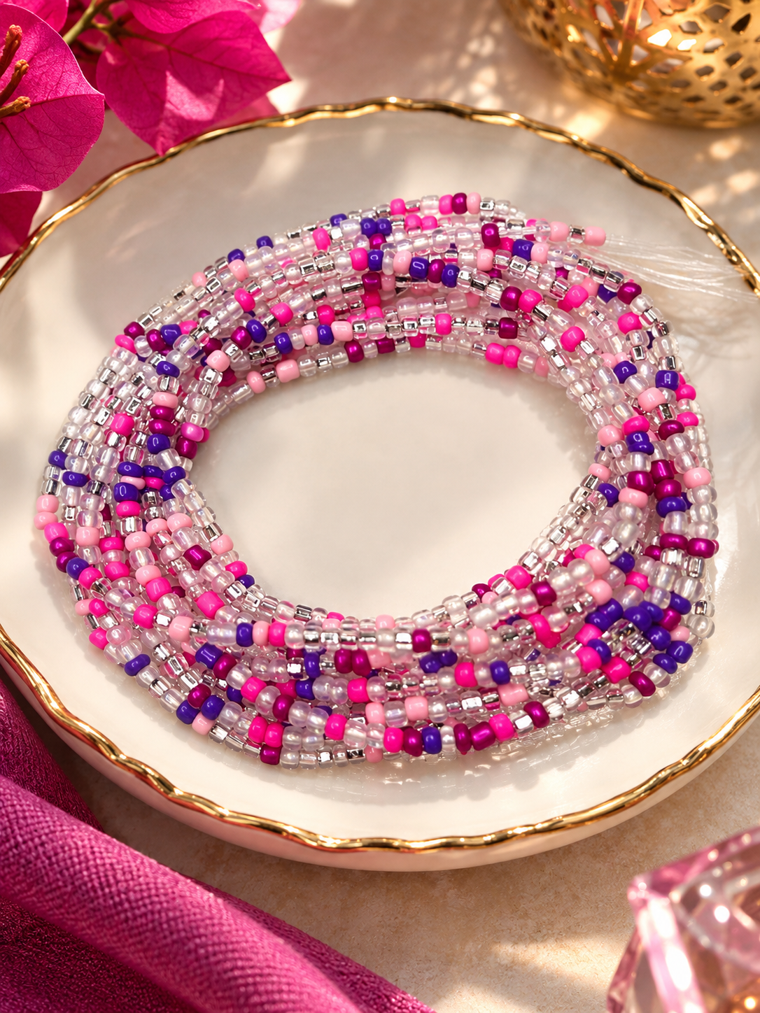 Pink Reign waist beads in fuchsia, rose pink, purple, and clear tones arranged on a dish