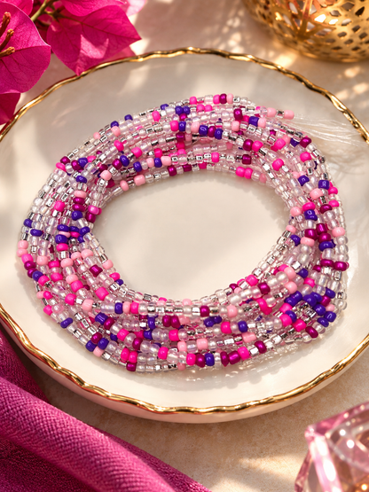 Pink Reign waist beads in fuchsia, rose pink, purple, and clear tones arranged on a dish