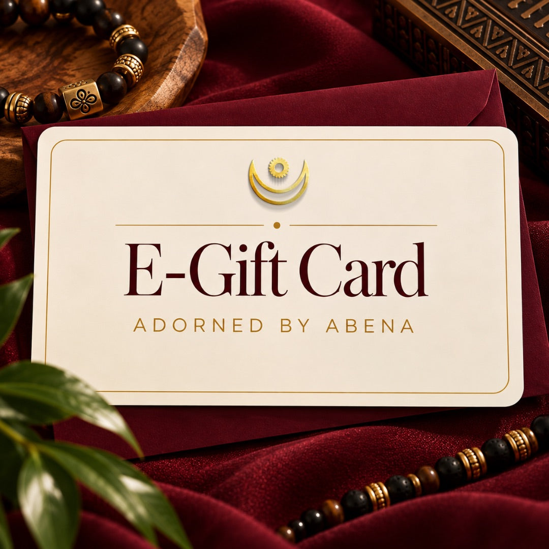 Adorn Him E-Gift Card in ivory and gold against burgundy fabric, masculine beaded bracelet, and wooden accents